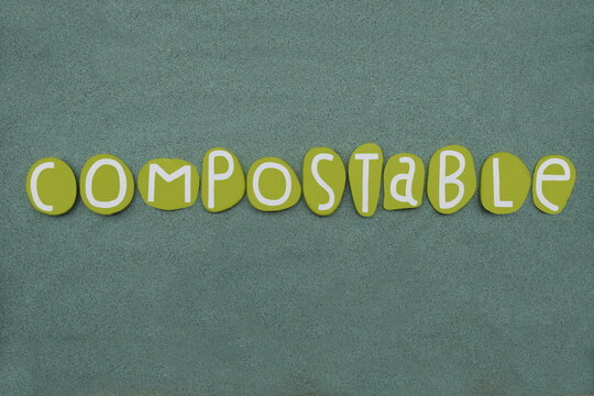 Compostable of organic matter, especially kitchen waste, able to be made into compost, creative word composed with green colored stone letters over green sand