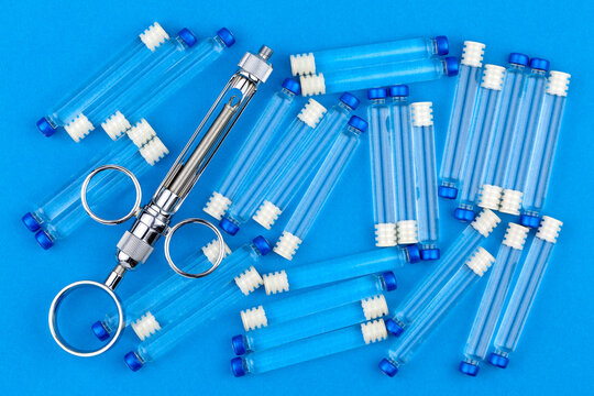 Metal syringe for local anesthesia and many carpules with anesthetic on a blue background.