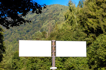 Two blank billboards for advertising on the background of a mountain covered with forest.
