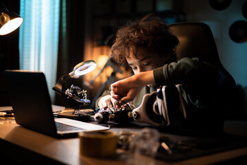 A young DIYer builds a robot. Child sits at desk and connects cables, toy electronics, solders wires, boy is interested in robotics