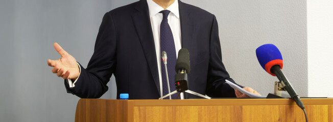 Man - politician, lawyer or official gesturing with his hands, holding documents and speaking from...