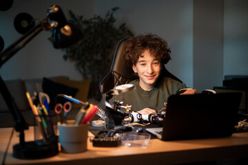Fototapeta na wymiar A boy works to create a fully functional robot from scratch. A clever teen solders cables at his desk, repairing the wiring of electronic equipment.