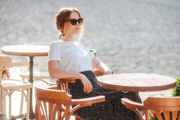 Stylish girl in sunglasses, white t-shirt and polka-dot skirt relax on the summer terrace