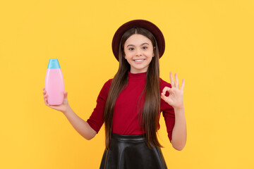 ok. happy girl in hat hold shampoo. presenting cosmetic product for teen.