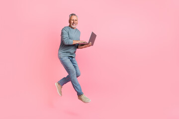 Photo of cute man pensioner dressed grey shirt jumping typing modern device empty space isolated pink color background