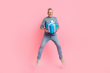 Full length body size view of handsome trendy grey-haired man jumping holding gift congrats isolated over pink pastel color background