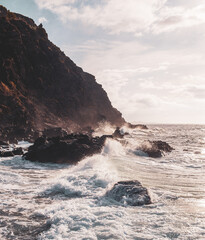 Stormy ocean sea water drops in cliffs and big waves come to the short in sunset or sunrise in blue and orange colors