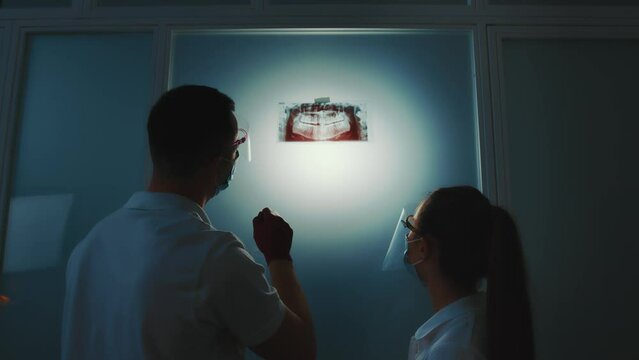 Two dentists look at a panoramic X-ray of the tooth gap in a dark room.