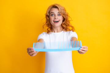 Funny excited amazed portrait of redhead woman with a comb, isolated on yellow background. Women hair care.