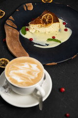 Classic cheesecake on a black background, dessert on a black background in a black plate, Latte coffee in a white cup
