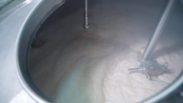 Mixing the produced beer wort ingredient inside mash tun at brewery. Foam is covering produced wort inside of the beer brewery tank. Brewing wort ingredient in the beer production equipment