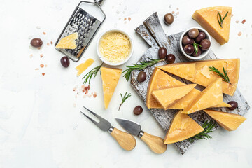 Parmesan cheese on a wooden board, Hard cheese, olives, rosemary and metal grater on a light background. place for text, top view