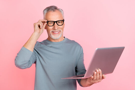Photo of dreamy clever man pensioner dressed grey shirt glasses typing modern device empty space isolated pink color background