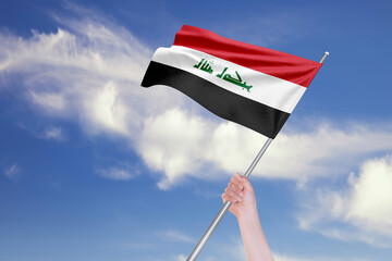 Female Hand is Waving Iraqi Flag Against Blue Sky with Clouds