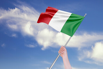 Female Hand is Waving Italian Flag Against Blue Sky with Clouds