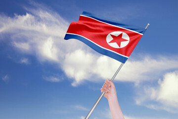 Female Hand is Waving North Korean Flag Against Blue Sky with Clouds