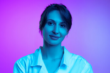 Young beautiful woman in white shirt isolated over purple studio background in neon light. Concept...
