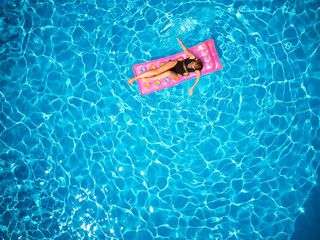 Fit pretty girl in bikini chilling on inflatable pink mattress in swimming pool. Slim hot woman in...