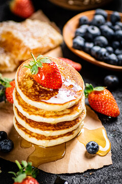 A pile of pancakes with berries and honey. On a black background. High quality photo