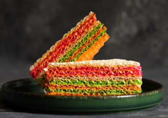 Colorful pieces of waffle cake with condensed milk on a ceramic plate on dark background. Close up.
