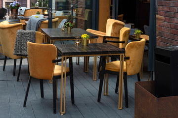 Empty tables with flowers in outdoor cafe or restaurant. Tables and chairs at sidewalk cafe. Touristic setting, small bouquets on cafe table, sidewalk cafe furniture.