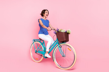 Full body photo of funky young brunette lady ride bicycle wear blouse pants footwear isolated on pink background