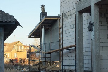 white brick wall of an unfinished private house and gray metal wooden scaffolding on the street