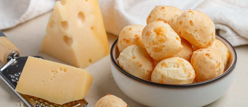 Freshly baked homemade cheese buns in a white plate on a light background close-up. Brazilian cheese bread. A gourmet snack. Delicious pastries. Selective focus, banner