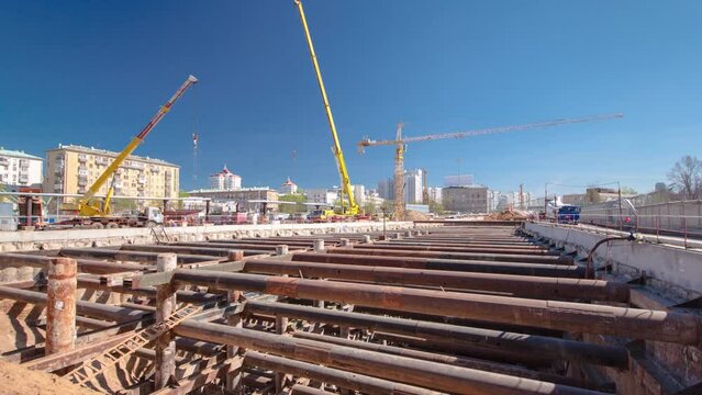 A large huge ditch pit tunnel with cranes timelapse. Reinforcing structures from thick iron pipes of beams and structures at the construction site of the underground metro station line.