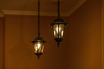 Fototapeta na wymiar Two vintage electric lighting lanterns hang on chains and glow on an orange background