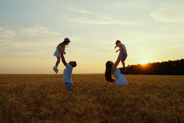 Family having fun in wheat field at sunset. Parents throwing children up in the air. Happy people enjoying time together in nature. Concept of love