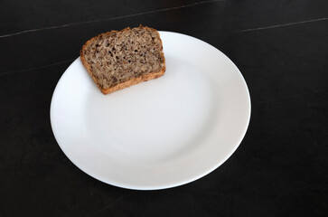 Bread on a white plate on a black table. Bread for lunch. To eat bread