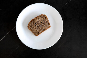Bread centered on a white plate on a black table. Bread for lunch. To eat bread
