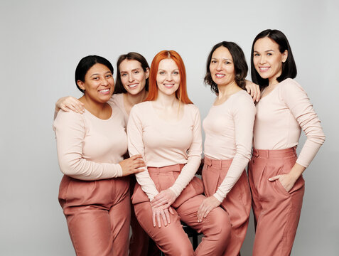 Portrait Of Smiling Interracial Women In Same Pink Outfits Standing Together Against Isolated Background