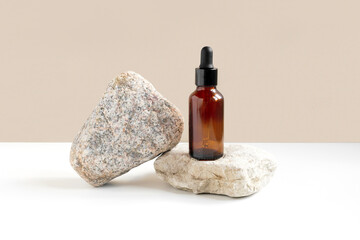 Dark amber glass bottle standing on stone. Natural skin care SPA beauty product design. Mineral organic oil cosmetics on beige background. Mock-Up. Oily pipette. Face and body treatment. Front view