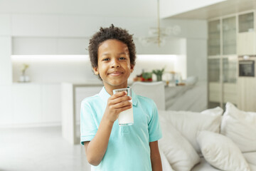 Little kid boy drinking milk in white home interior