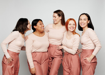 Group of positive interracial women in same clothes embracing each other and laughing together