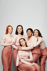 Group of cheerful multi-ethnic women having close connection embracing each other against white wall