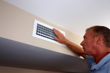 White Male Hand on a White Air Duct Vent Grille on a Beige Wall