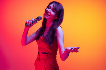 Naklejka premium Young excited girl, student with long hair singing isolated on orange background in neon light, filter. Concept of emotions, youth, beauty