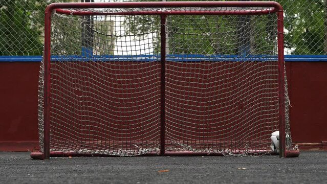 Poor looking soccer ball roll in small unprotected goal, pass line and stop, slow motion shot, no people. Deflated ball, beat-up net of gate have holes