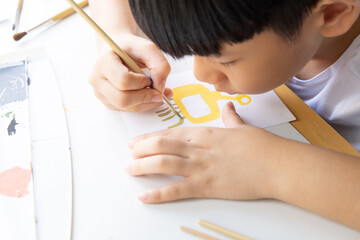 Close up of cute Asian little boy drawing and painting his imagination monster character on white...