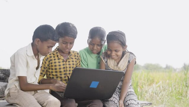 group of village kids busy using laptop near paddy field - conept of online education, technology and learning.