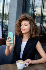 young pretty curly haired business woman talking by smart phone in cafe