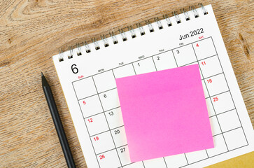 Blank sticky note on June 2022 desk calendar on wooden background.