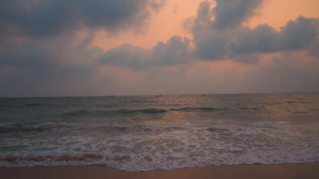 Wide angle slow motion shot of sea waves during the sunset at Colva Beach in Goa, India. Clouds above the sea during the sunset. Beautiful beach sunset background. Summer holidays at beach concept.	