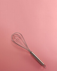 Steel whisk flat lay top view. Confectionery cooking concept with copy space on bright pink paper background.