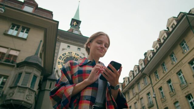 Girl uses Smartphone mobile App near Bern Landmark Clock Tower Zytglogge, Switzerland. Young Woman types text message near Swiss Historic Monument in European Capital. 4K low angle hero shot