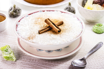 rice pudding bowl, homemade pudding made from ground rice, sweetened with cinnamon powder and cinnamon bark. Rural Brazilian sweets in the background, typical June festival food
