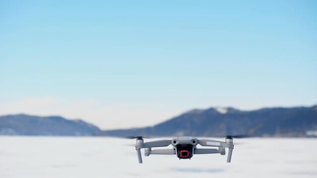 in the frame from the bottom up, a drone appears against the background of mountains in winter, slowly rises up, turns around and flies away. aerial monitoring from a height. slow motion. close-up.